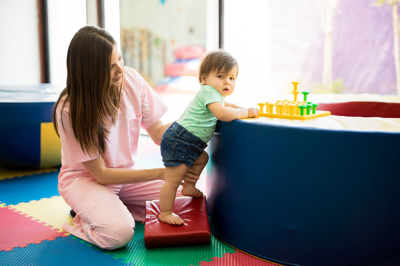 Portrait of a Hispanic baby standing and practicing maintaining balance while playing in a children therapy center